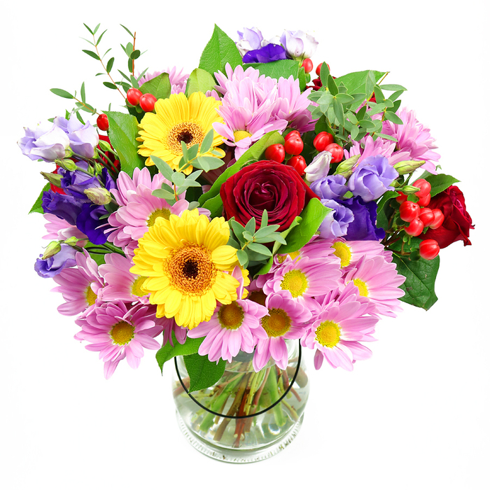 This image shows a generous floral arrangement brimming from a clear glass vase, placed against a clean white background that lets each bloom stand out distinctly. At the centre, rich deep red roses curl in soft, velvety spirals, exuding timeless romance and becoming the natural focal point of the bouquet. Close to them, two bold yellow gerbera daisies with dark brown-orange centres provide a dazzling contrast, their large, disc-like faces tilted charmingly at slightly different angles, giving the design energy and personality. Surrounding these key flowers is a profusion of soft pink daisies or chrysanthemums, clustered closely to form a halo of delicate colour; each small flower has many slender petals and a subtle yellow centre, adding both volume and lightness. Woven throughout the composition, purple and lavender lisianthus blooms introduce layers of cool, refined colour. Some of the lisianthus flowers are fully opened, revealing ruffled, bell-shaped petals, while others remain as elegant buds, suggesting freshness, as though the bouquet has just arrived from a florist near St John's Wood High Street. Tucked between the petals, vivid red hypericum berries provide rounded, glossy accents, punctuating the softer textures with a playful, contemporary twist. A mix of green foliage completes the arrangement: broad, dark-toned leaves support the base and lighter, more delicate greenery lifts the shape upward, creating balance and a sense of natural movement. Through the transparent vase, neatly cut stems can be seen resting in clear water, indicating careful preparation and conditioning. The overall effect is of a joyful, celebratory bouquet-ideal for birthdays, anniversaries, or simple acts of kindness-ready to brighten a living room overlooking Regent's Park or a quiet apartment nestled in St John's Wood.